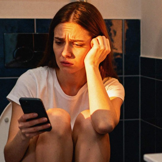 Femme sur les toilettes sur son téléphone qui a mal au ventre