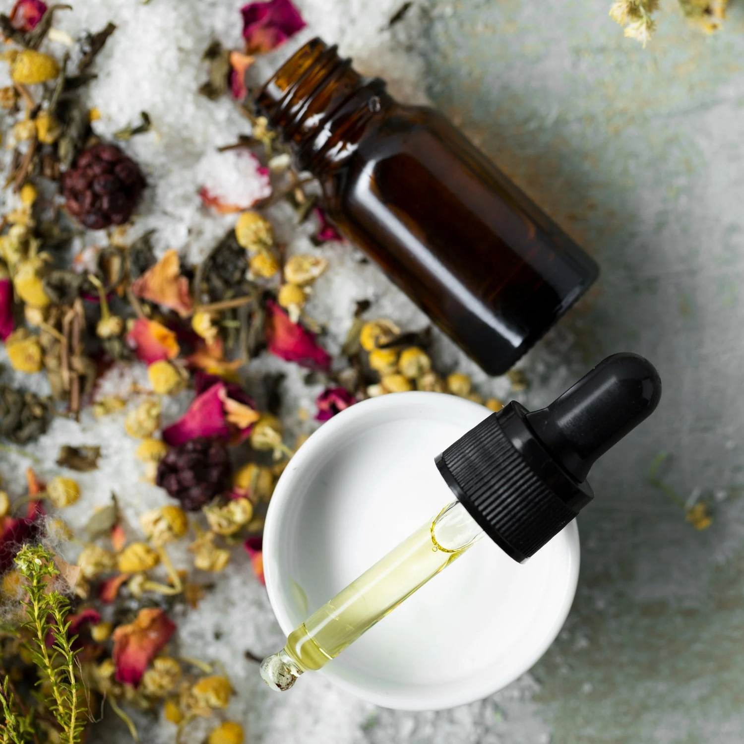 Flacon compte goutte ouvert avec de l'huile, posé sur un bol avec des fleurs